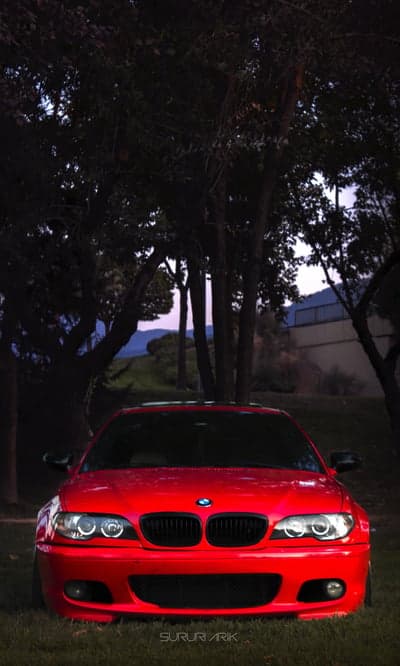 Red BMW E46 M3 parked under trees at dusk