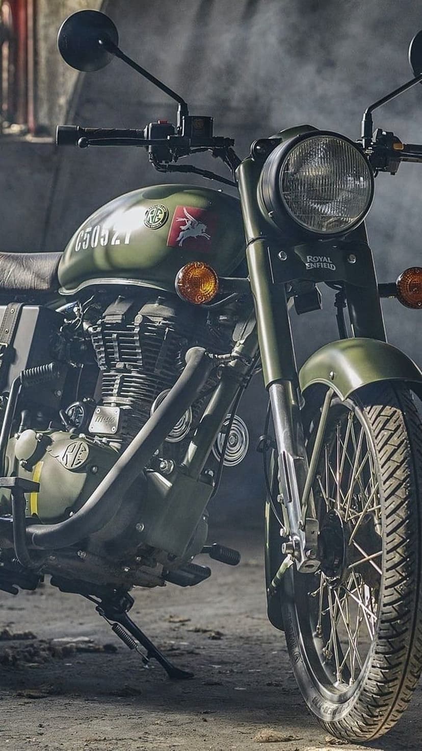 Army green Royal Enfield motorcycle featuring a round headlight and engine details in a misty studio setting.