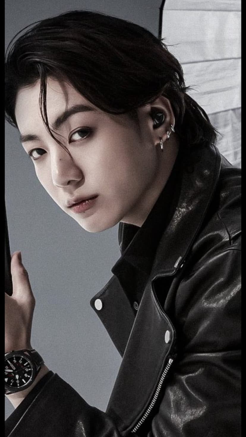 Jungkook from BTS wears a black leather jacket and silver earrings in a sharp, close-up fashion portrait.