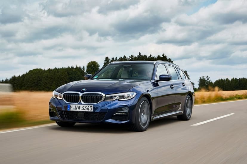 Dark blue BMW sports wagon driving on a road with motion blur, green trees, and a cloudy sky background.