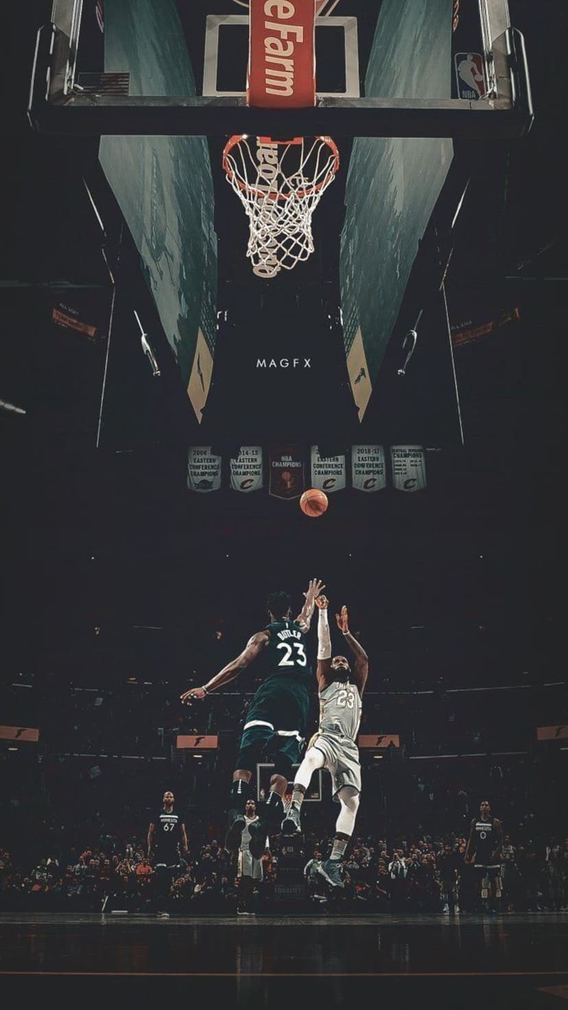 Two basketball players leap toward a rim and backboard in a dark arena with glowing overhead stadium lights.