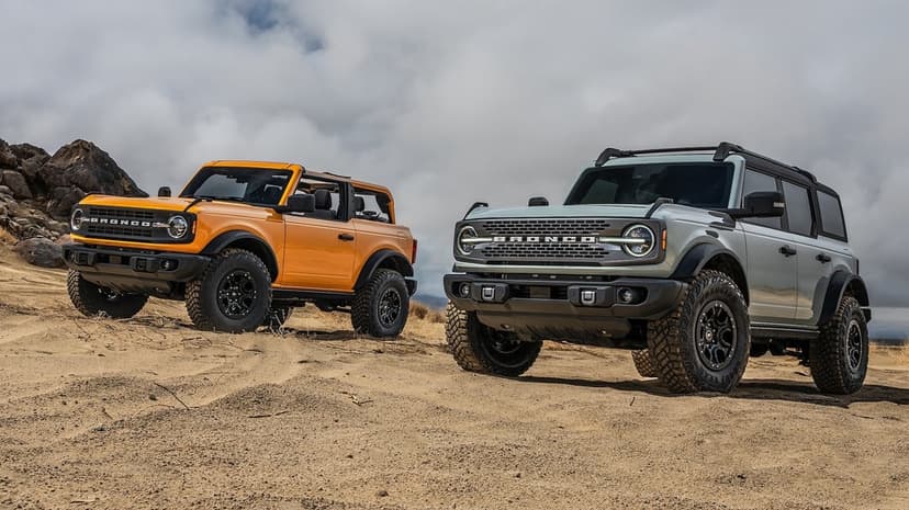Yellow and grey Ford Bronco SUVs parked on a sandy desert hill under a dramatic cloudy sky.