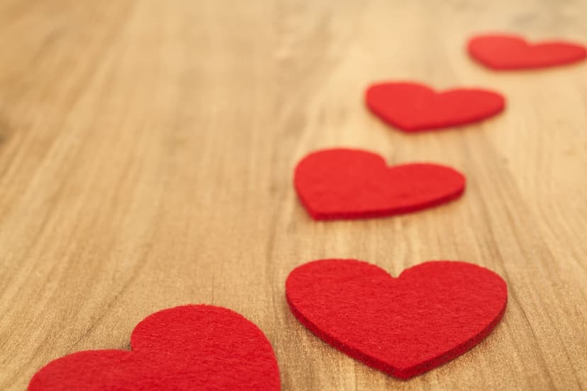 Three red felt hearts on a wooden board with shallow depth of field and warm natural lighting for a cozy mood.