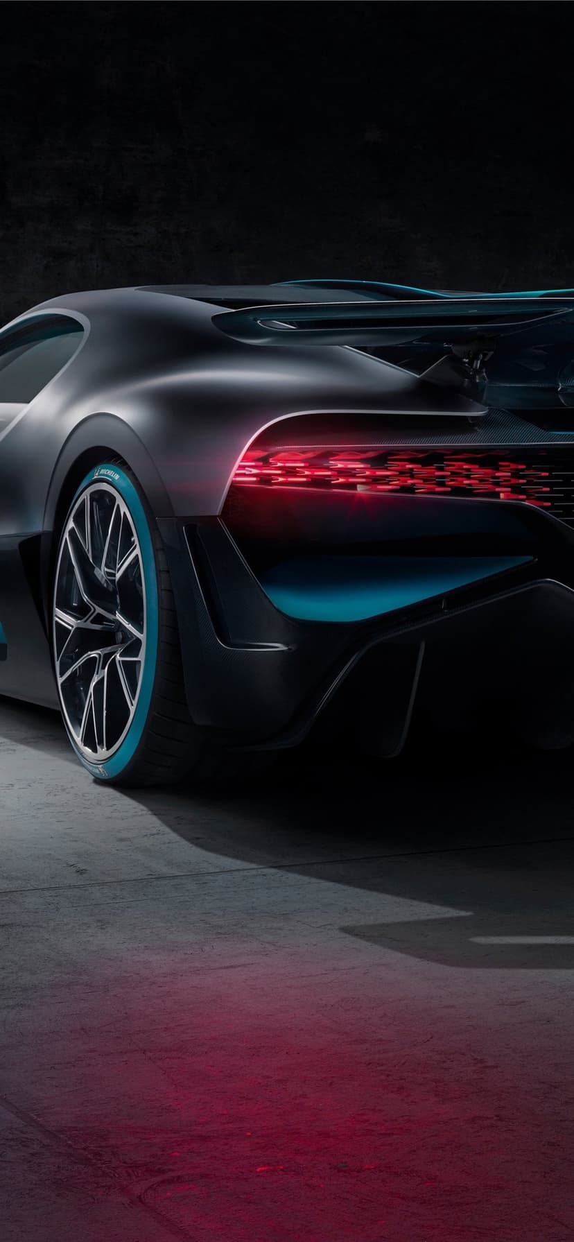 Rear view of a matte black Bugatti Divo with glowing red LED lights and turquoise tire accents.