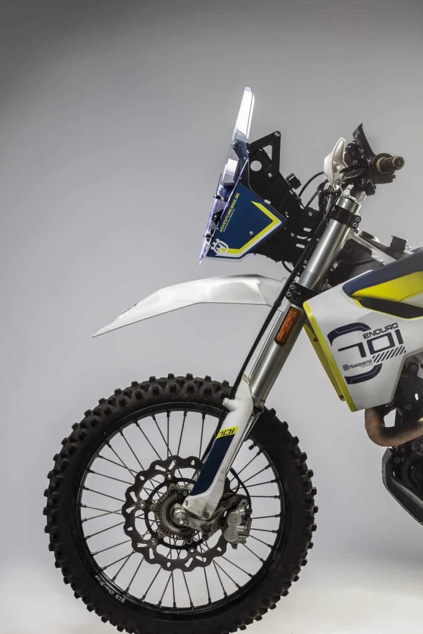 Husqvarna 701 Enduro rally bike with blue decals and knobby tires captured in profile against a gray background.
