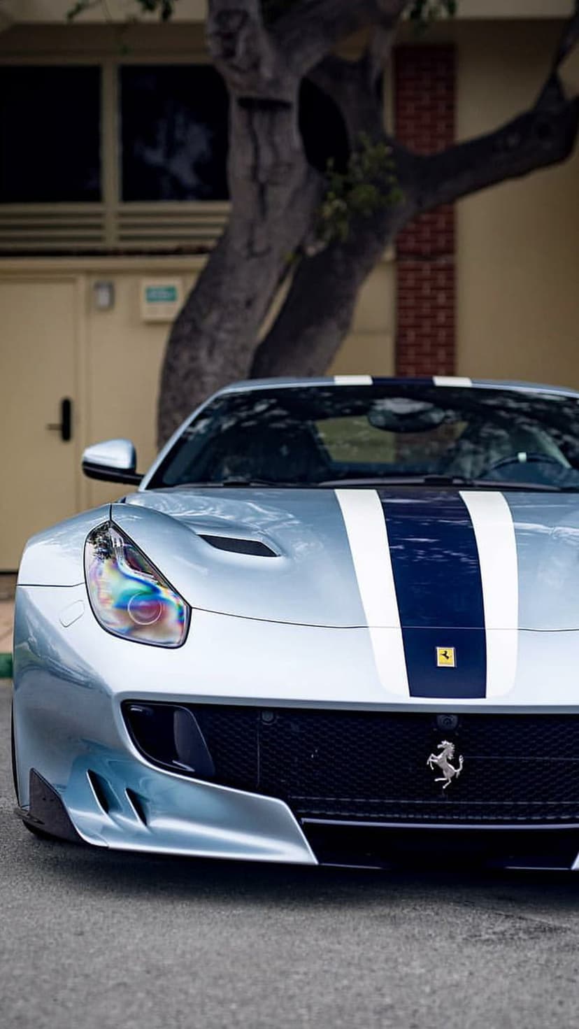 Light blue Ferrari front view with navy racing stripes and yellow prancing horse badge in an outdoor setting.