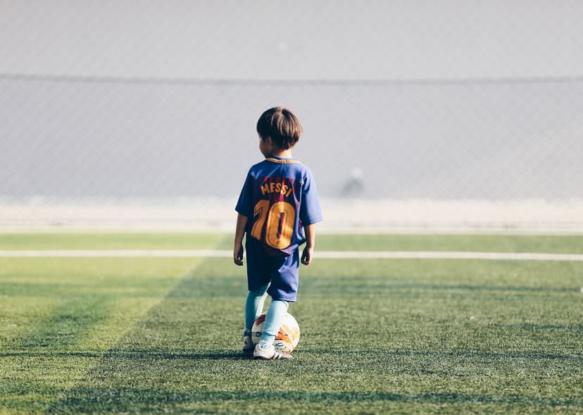 Young boy wearing a blue number ten soccer jersey stands on a green field with a football at his feet.