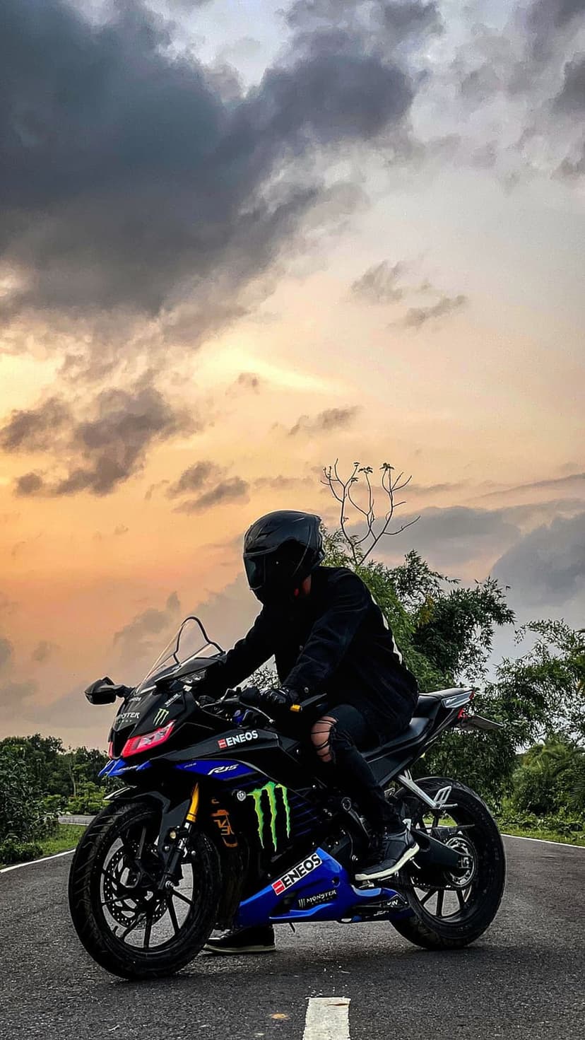 Motorcyclist in black gear riding a sportbike on a road against a dramatic orange sunset with golden clouds.