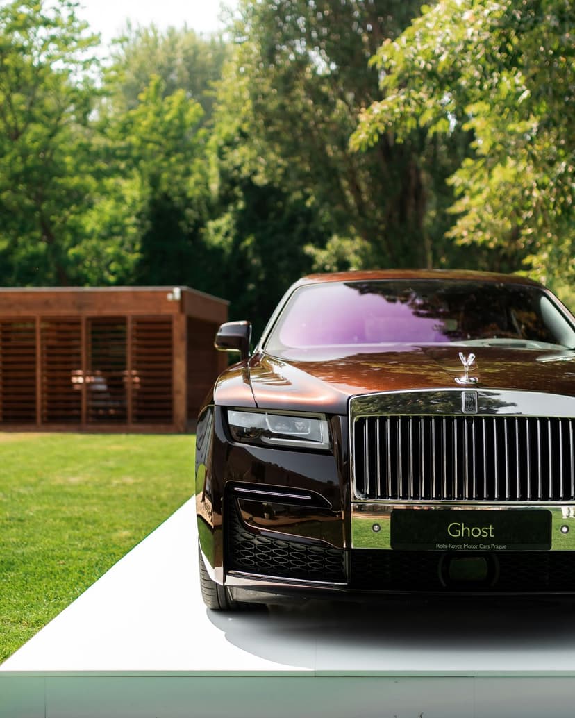 Rolls-Royce Ghost in brown sits on a white platform featuring the iconic chrome grille and Spirit of Ecstasy ornament.