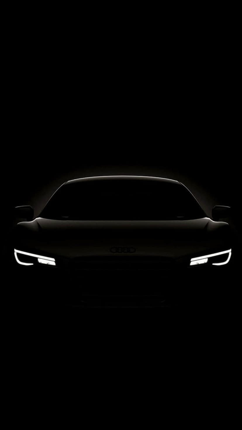Audi R8 front grille and glowing LED headlights emerge from a pitch-black background in a minimalist silhouette.