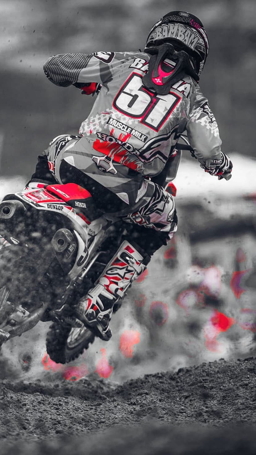 Motocross racer number 51 on a Honda motorcycle kicks up dirt in a selective color red and grayscale scene.