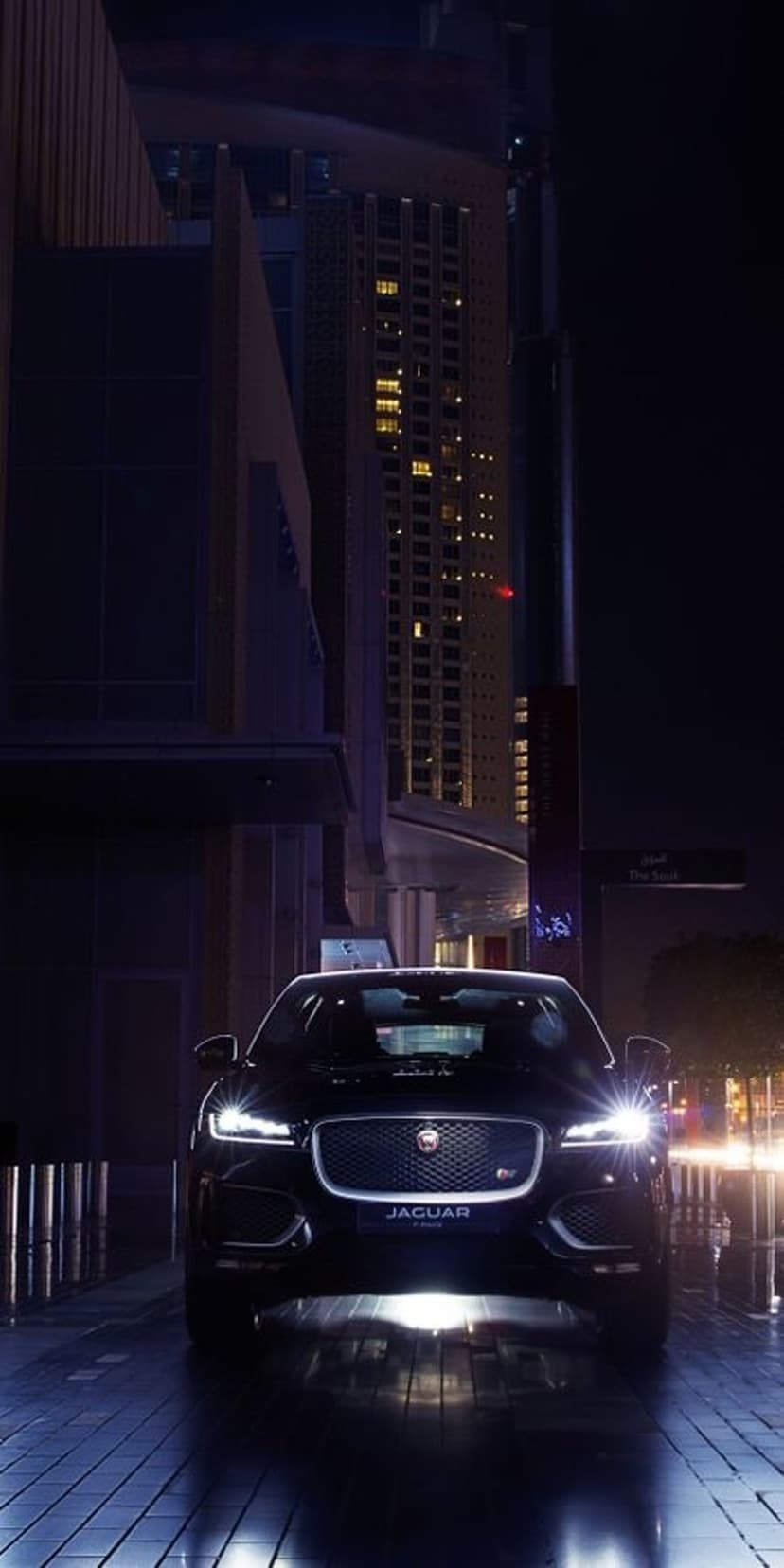 Black Jaguar F-PACE SUV on a wet city street at night with glowing headlights and reflected urban lights.