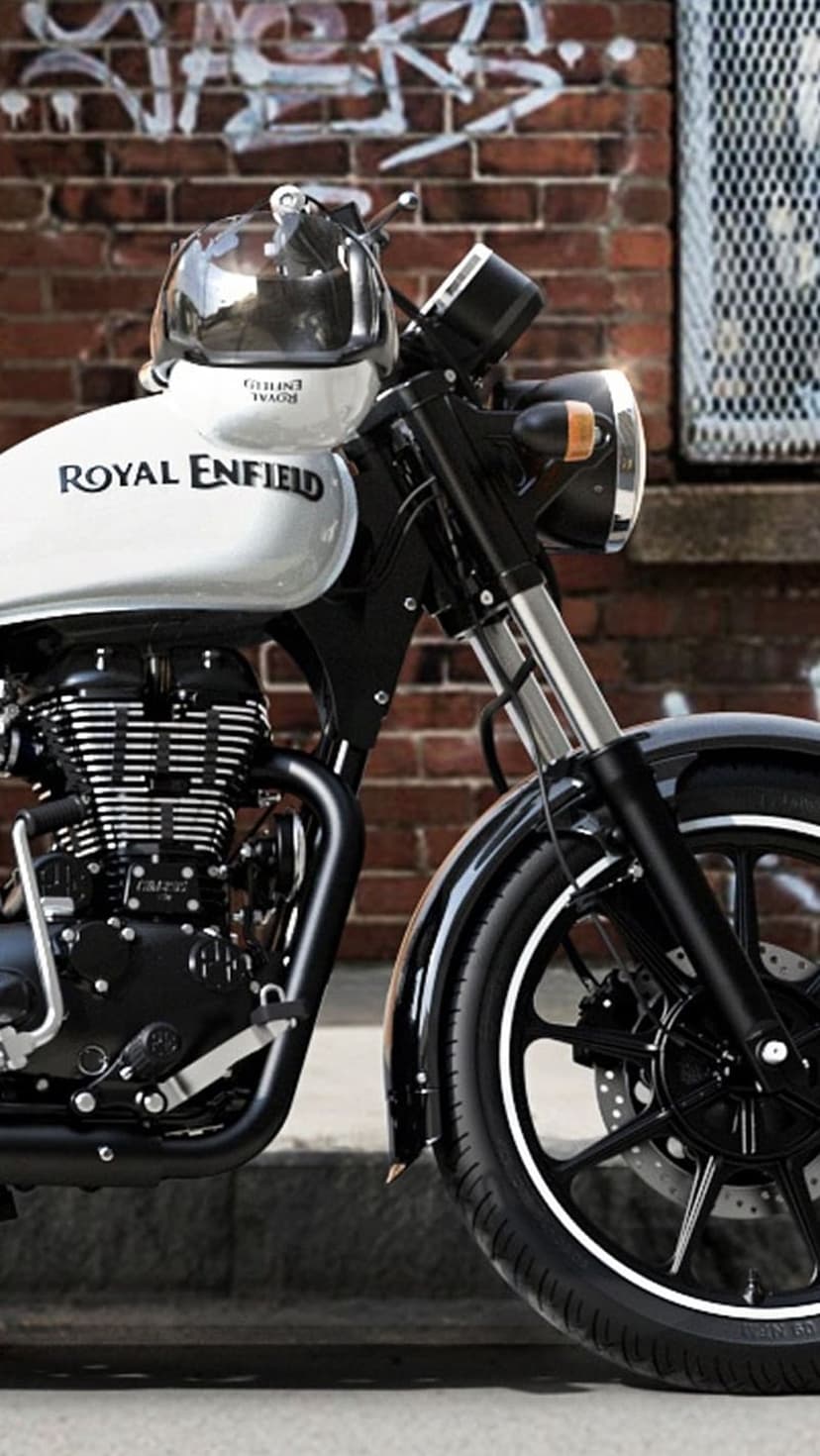 White Royal Enfield motorcycle with a helmet on the tank parked against a colorful graffiti brick wall.
