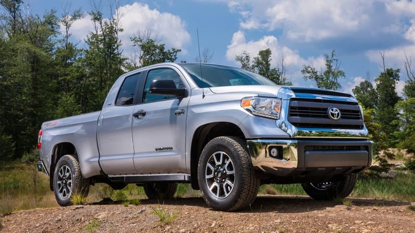 Silver Toyota Tundra pickup truck parked on a dirt hill with a forest and cloudy blue sky background.