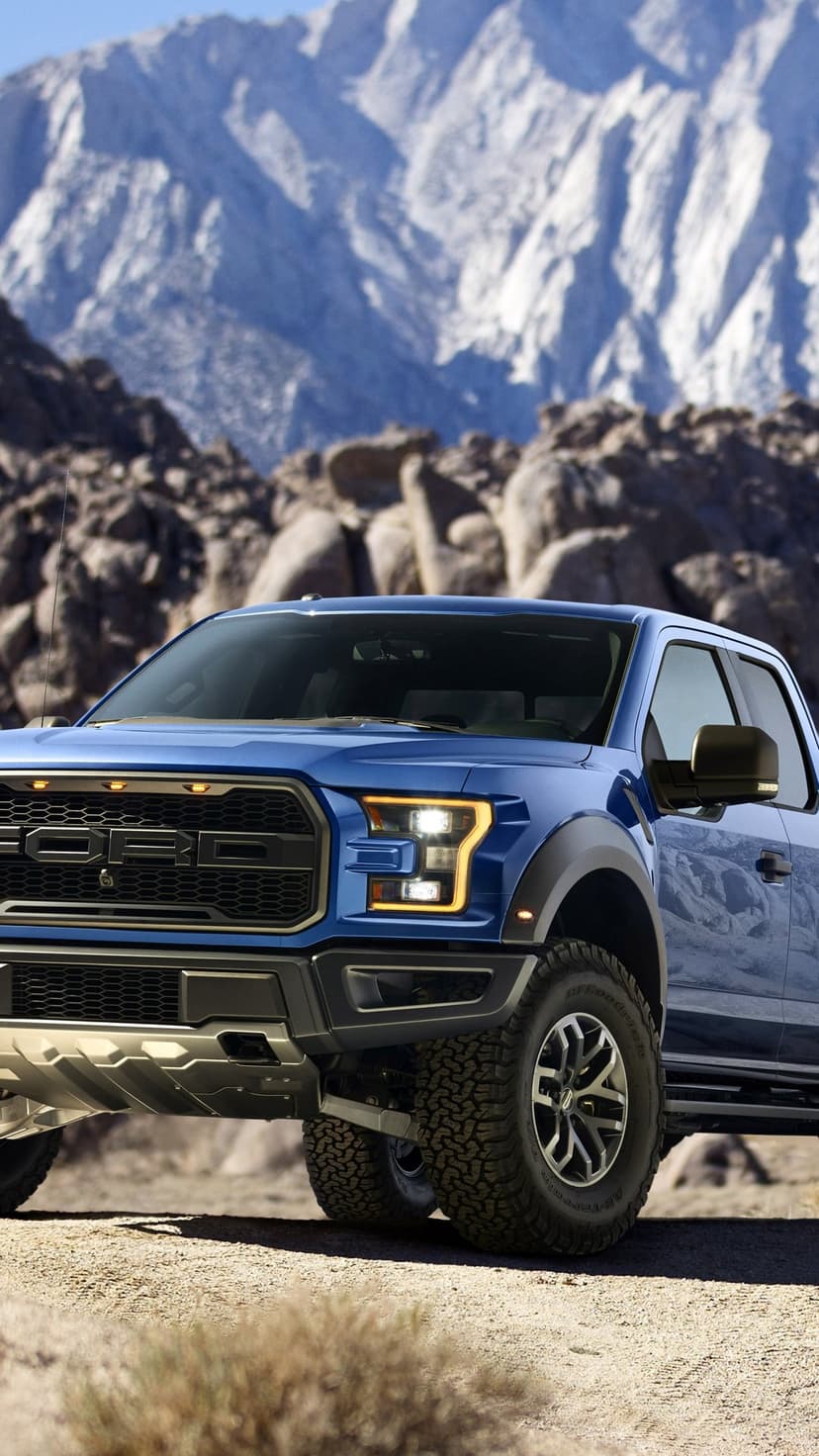 Blue off-road pickup truck with amber lights parked on a desert trail with towering mountains in the background.