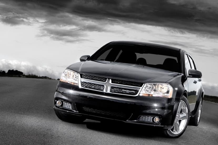 Black Dodge Avenger sedan with a chrome grille parked on an asphalt road under a dramatic, dark cloudy sky.