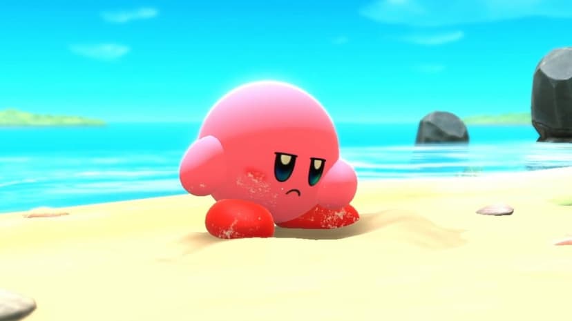 Pink Kirby sits on a sandy beach with a grumpy expression under a bright blue sky and turquoise ocean water.