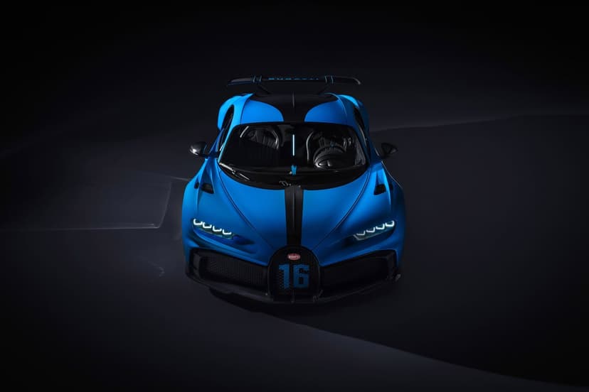 Blue Bugatti Chiron Pur Sport hypercar front view with glowing LED headlights on a black studio background.