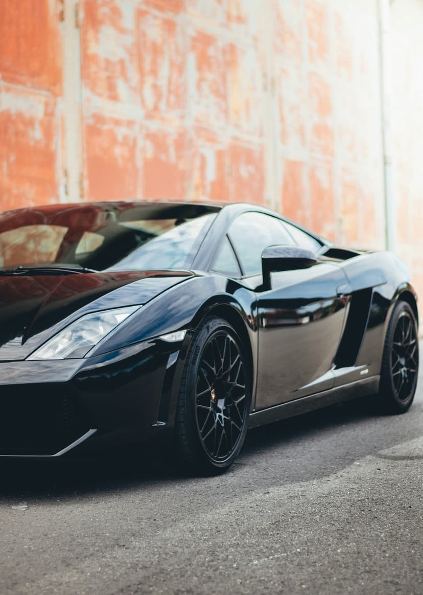 Black Lamborghini supercar with a glossy finish parked against a rustic orange wall showing low-angle details.