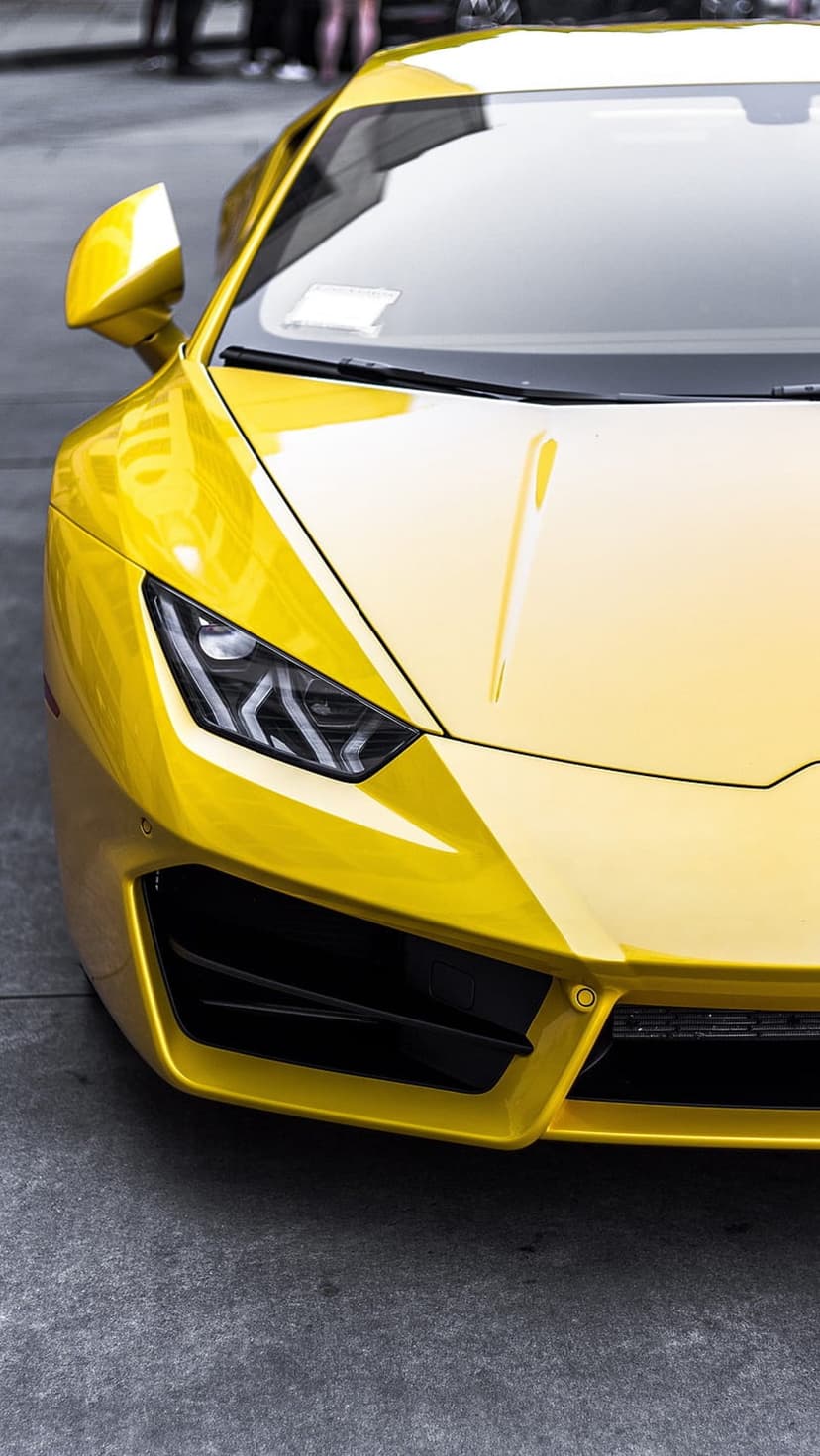 Yellow Lamborghini front end featuring sharp LED headlights and black air intakes on a gray asphalt background.