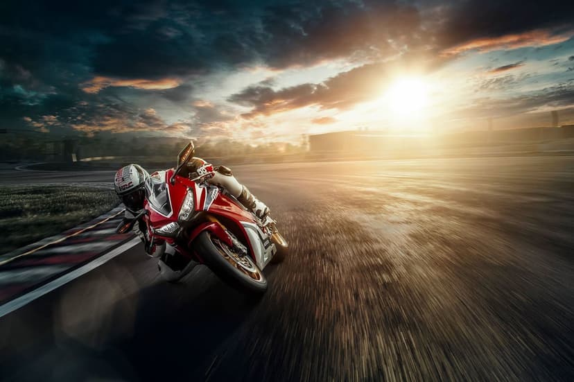 Red sportbike and rider leaning deep into a racetrack turn at sunset with motion blur and golden lighting.