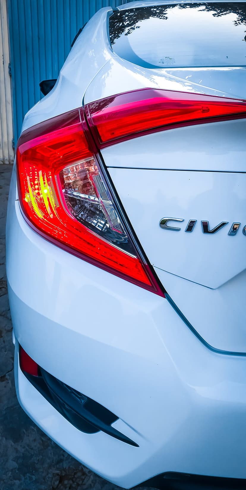 Honda Civic chrome badge and red LED tail light on a white car trunk against a textured blue studio wall.