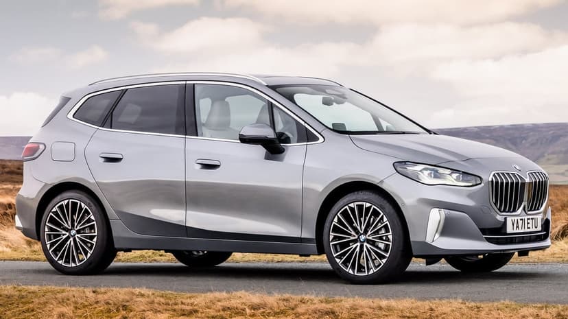 Silver BMW 2 Series Active Tourer profile on a rural road with hills and a cloudy sky in the background.