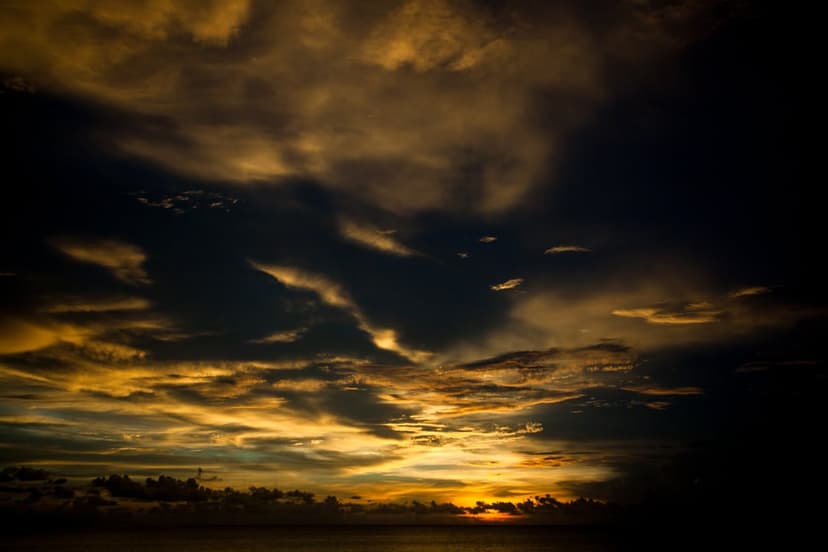 Golden clouds hover over a dark calm ocean horizon during a dramatic coastal sunset in a vertical landscape.