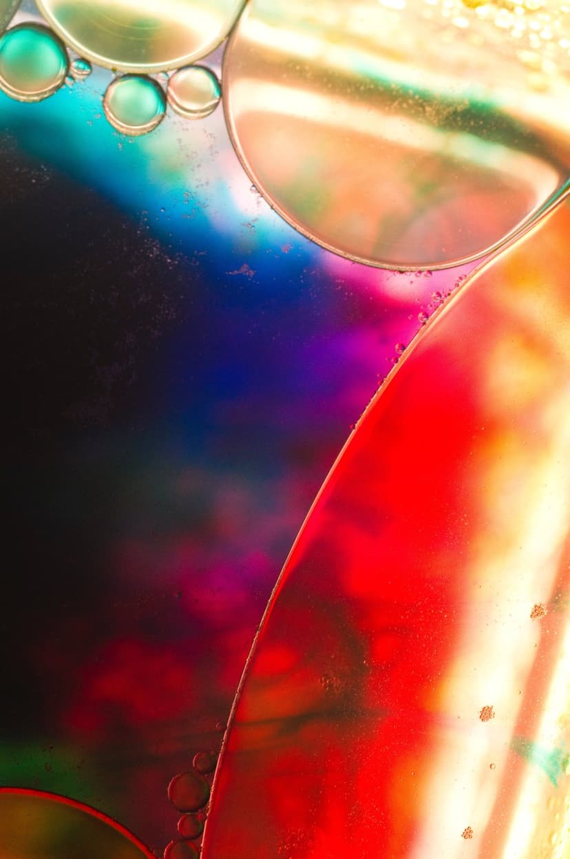 Iridescent oil bubbles float over a vibrant spectrum of red, blue, and green liquid in a macro photograph.