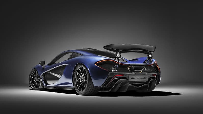 Rear view of a blue carbon fiber McLaren P1 hypercar with a large wing in a dark studio with floor lighting.