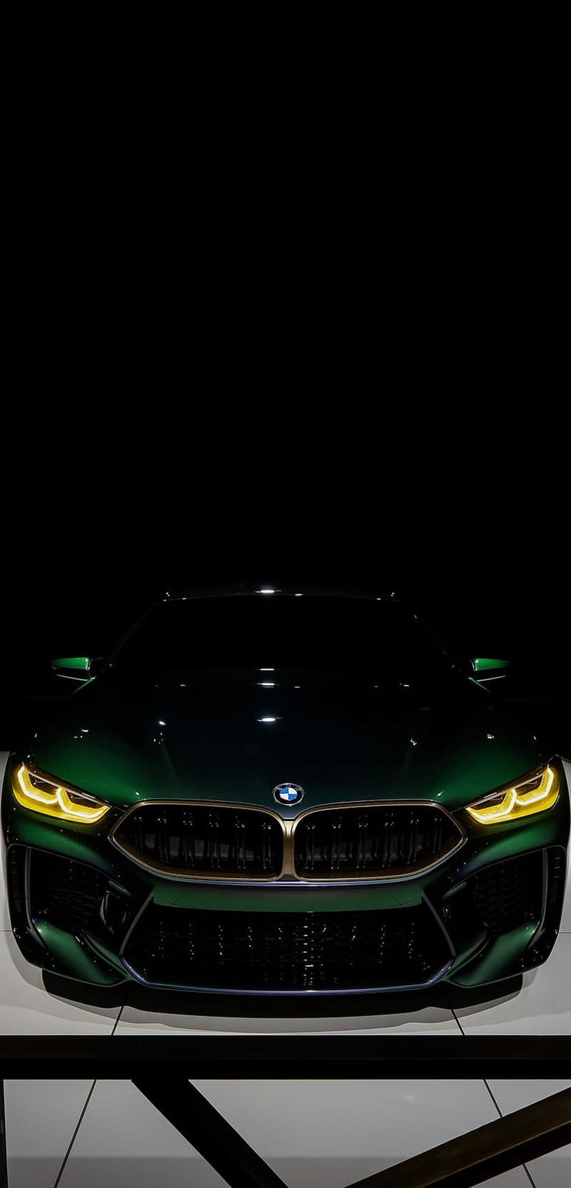 BMW M8 Coupe featuring yellow glowing headlights and a gold kidney grille against a dark minimalist background.