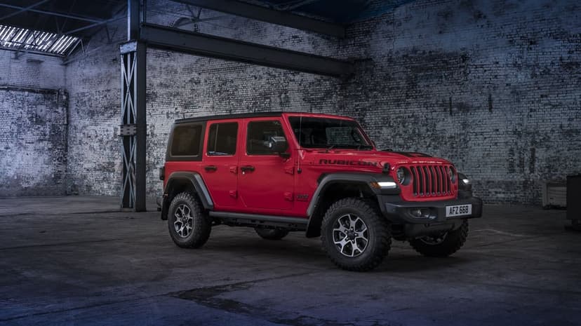 Red Jeep Wrangler Rubicon parked inside a dark industrial warehouse with white brick walls and concrete flooring.