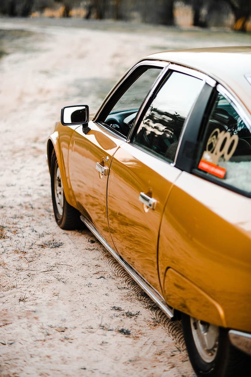 Golden Citroën CX parked on a sandy path with chrome accents and sky reflections in a low-angle shot.