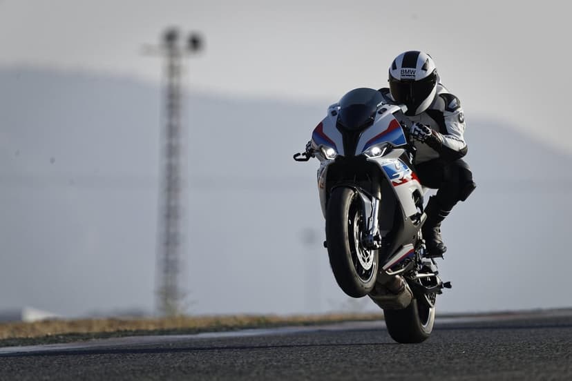 BMW S1000RR motorcycle performing a front wheelie on a racetrack with a rider in white racing leathers.