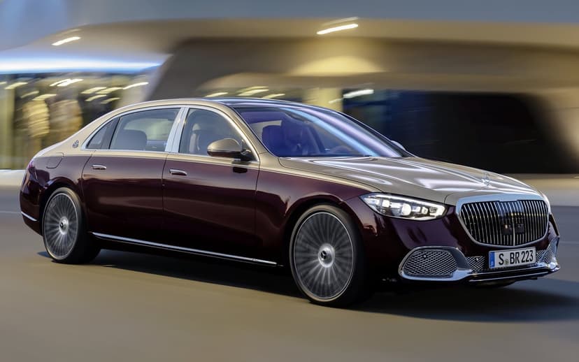 Two-tone burgundy and gold luxury sedan driving past modern buildings with motion blur and glowing headlights.