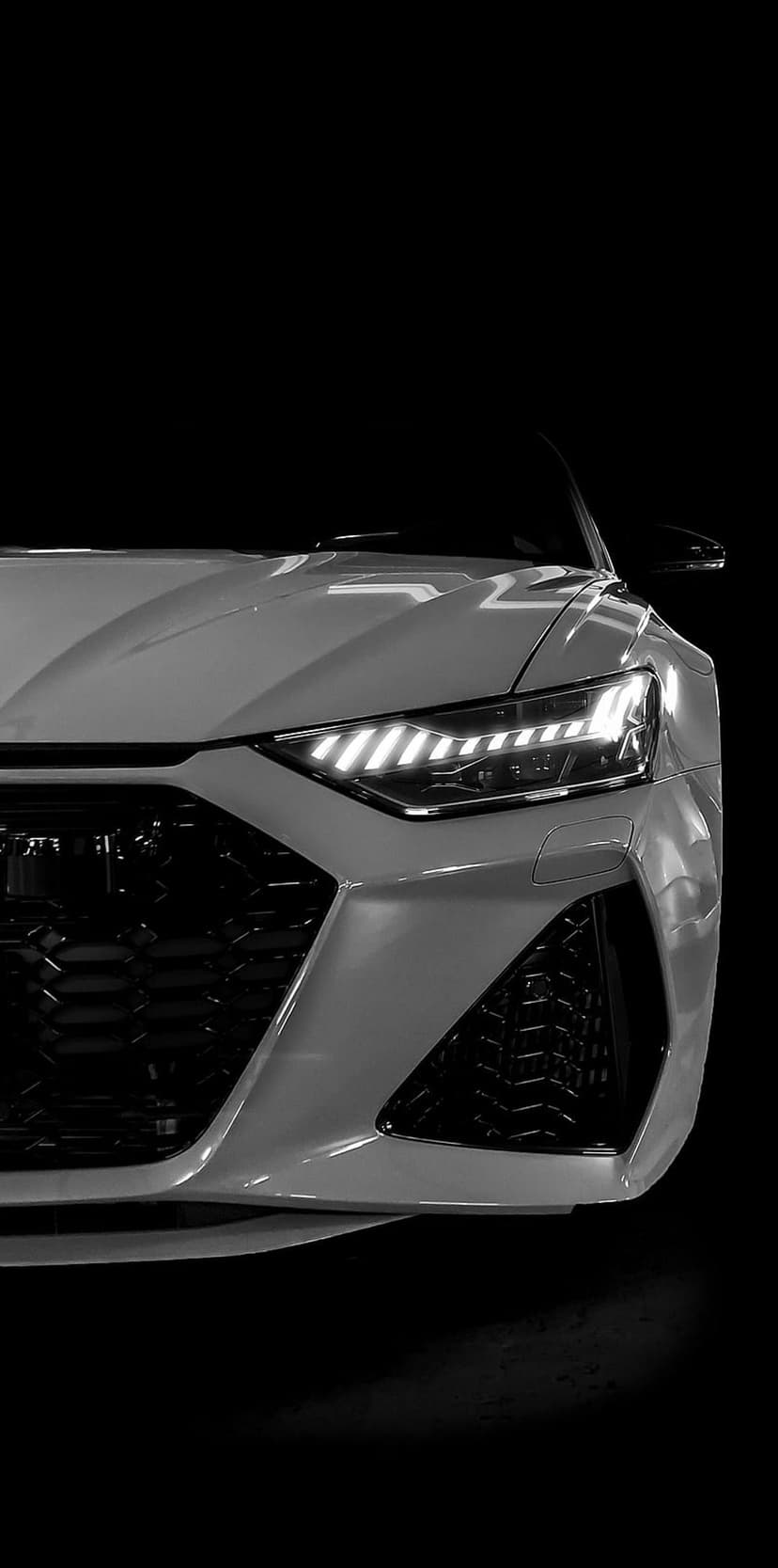 Audi RS6 Avant front grille and sharp LED headlights highlighted against a solid black background in monochrome.