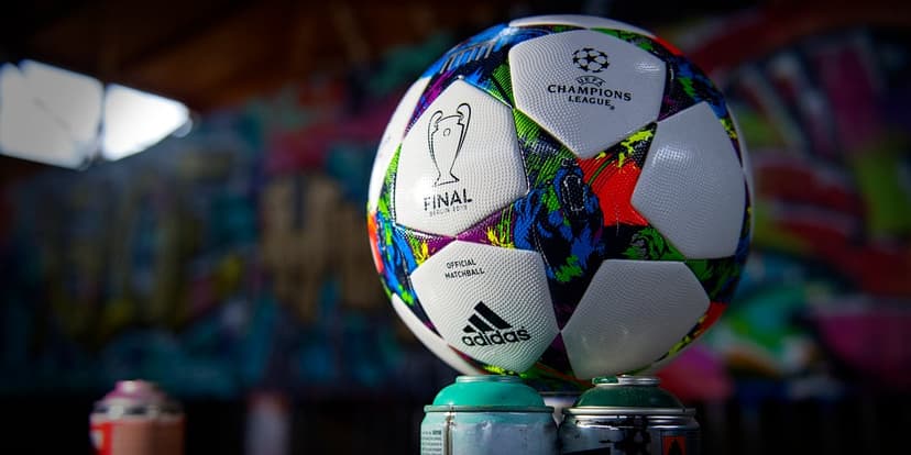 Adidas Champions League soccer ball sits on colorful spray paint cans against a blurred graffiti wall mural.