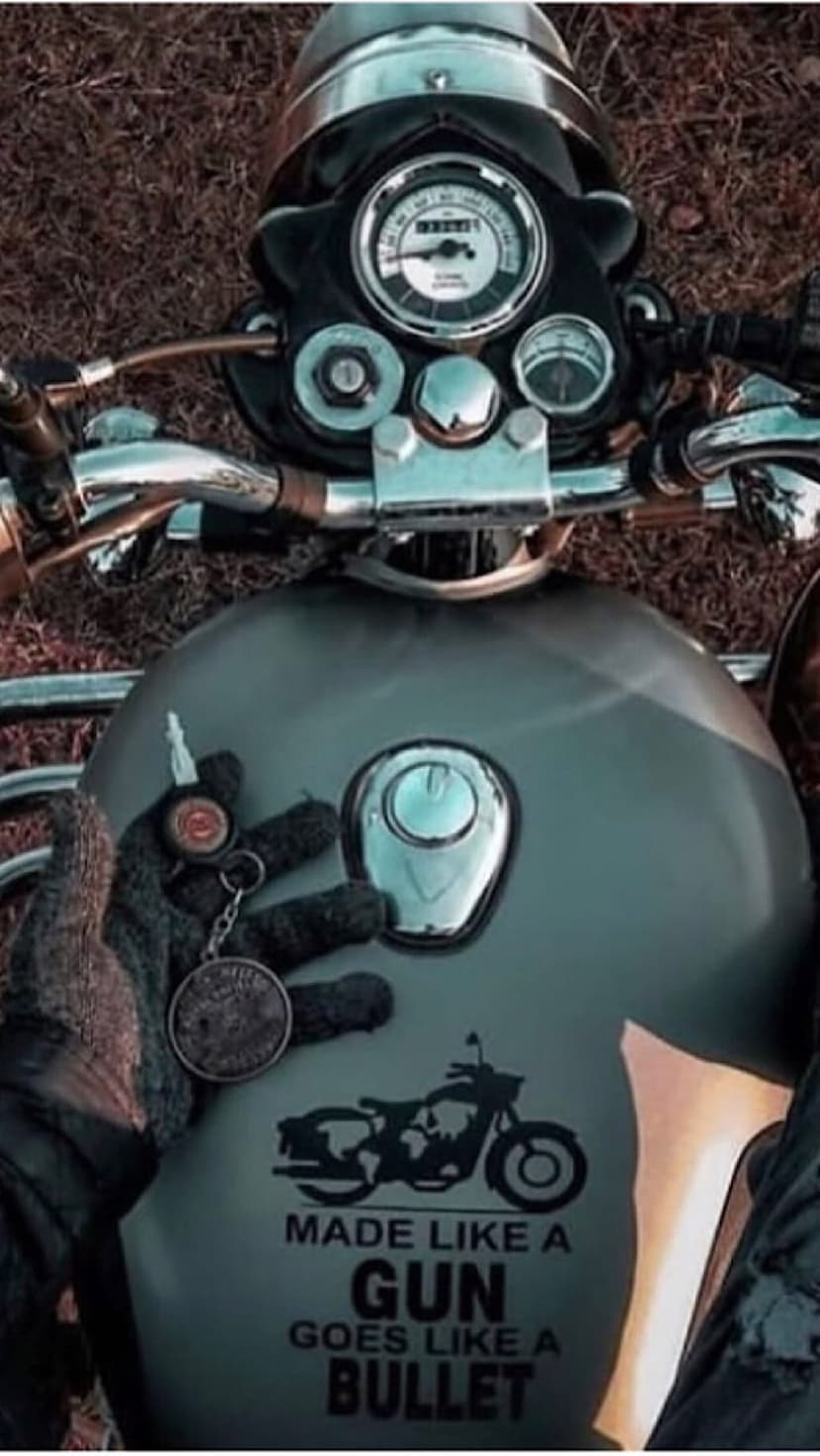 Biker hand holding ignition keys above a motorcycle fuel tank featuring a custom sticker and chrome accents.