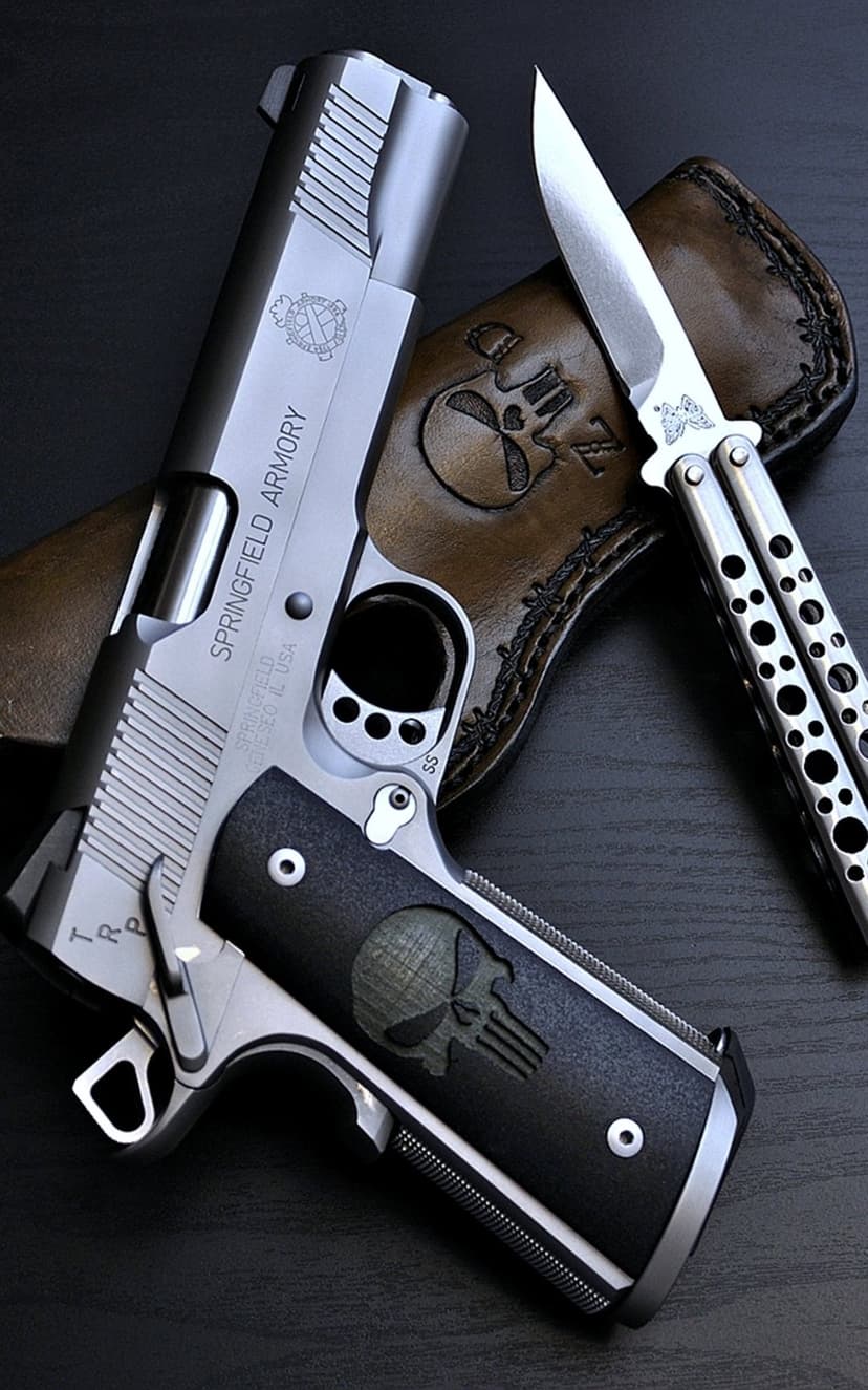 Springfield Armory 1911 pistol with skull grips rests beside a silver balisong knife and leather skull sheath.