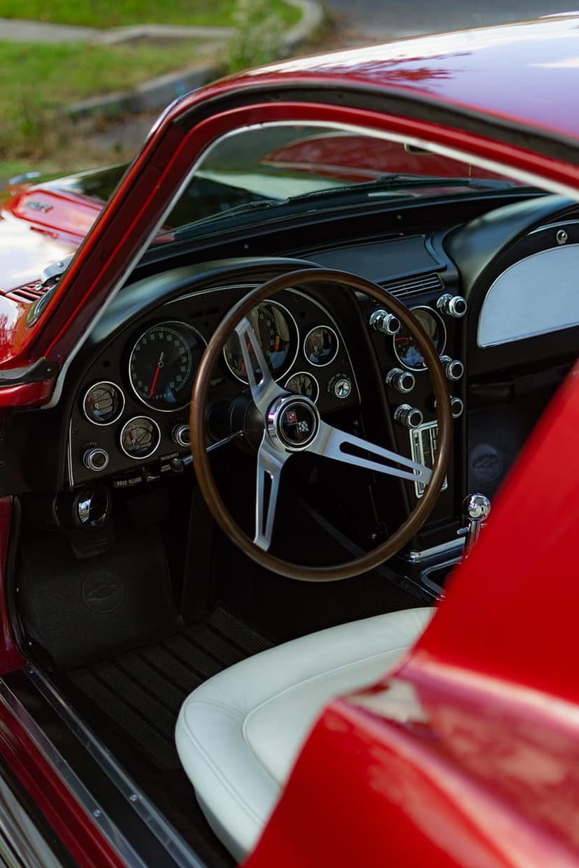 Red Corvette interior featuring a wood-rimmed steering wheel, chrome analog gauges, and a vintage dashboard.