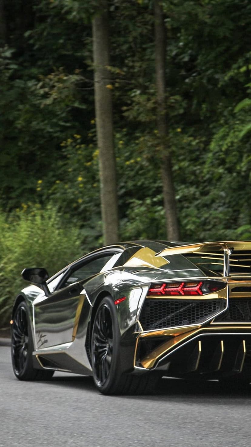 Gold-accented chrome Lamborghini Aventador rear view on a forest road surrounded by lush green trees and foliage.