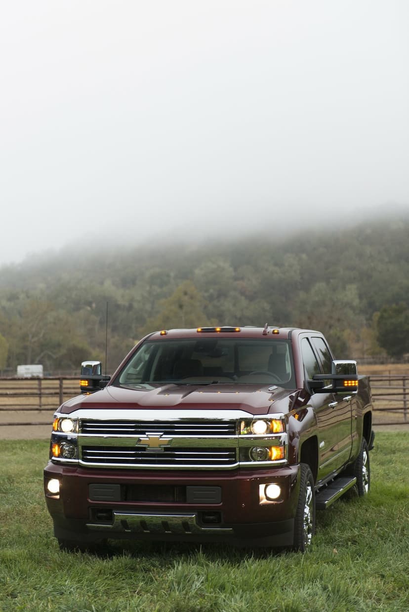 Front view of a maroon Chevrolet Silverado truck with lights on in a grassy field under a thick foggy sky.