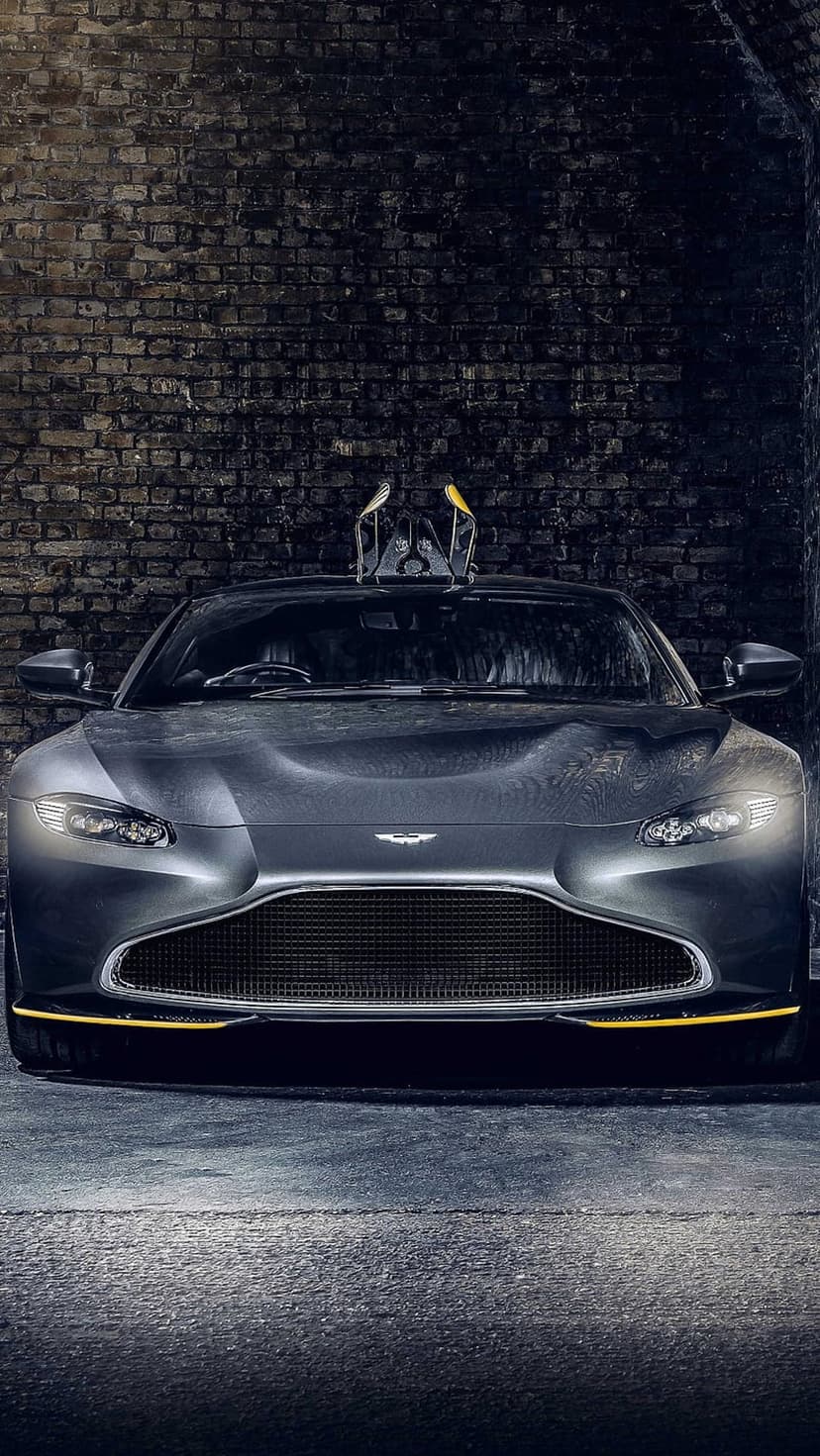 Aston Martin front grille and headlights with a flux capacitor prop on top against a dark brick wall.