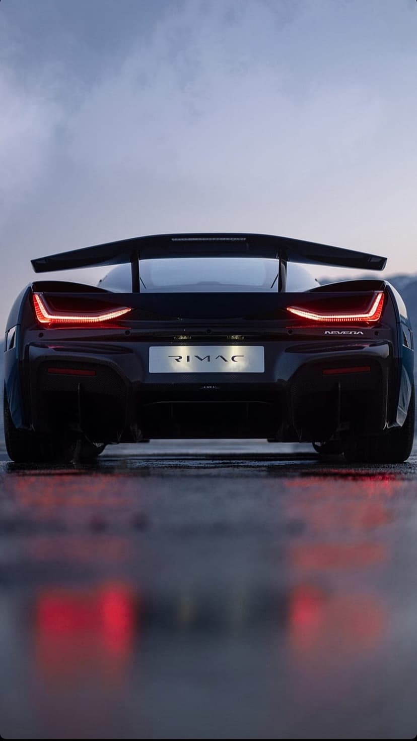 Rimac Nevera rear view with red LED taillights on a reflective wet surface under a dark moody sky at dusk.