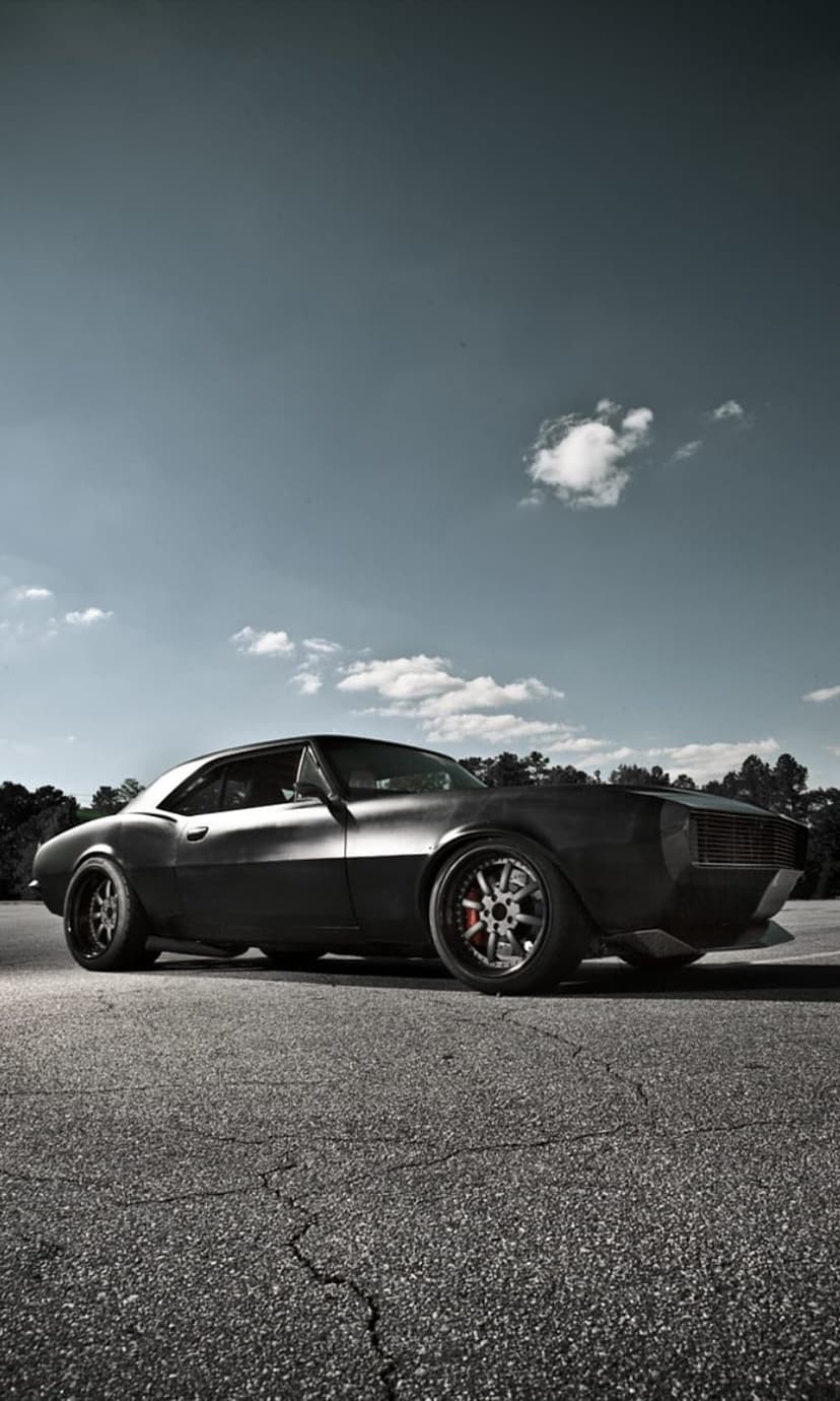 Matte black Chevrolet Camaro restomod on cracked asphalt under a cloudy sky with visible custom brake calipers.