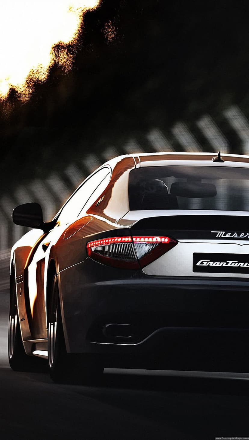 Maserati GranTurismo rear end with lit taillights on a blurred road during a vibrant orange sunset.