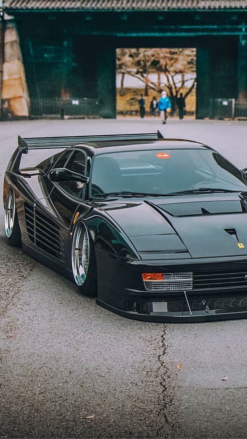 Black Ferrari Testarossa with a large rear wing and slammed stance parked before a traditional Japanese gate.