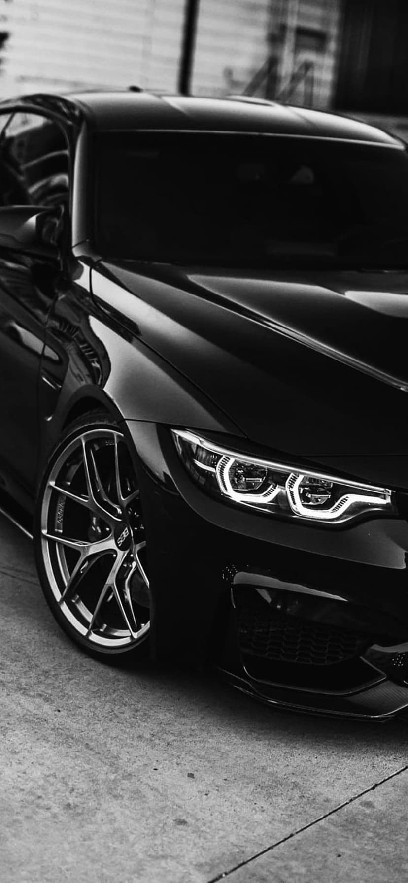 Black BMW M4 coupe highlights aggressive front styling, alloy wheels, and LED lights in monochrome tones.