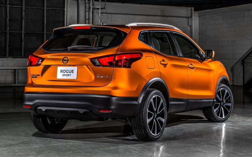 Rear view of an orange Nissan Rogue Sport SUV with lit taillights in a dark industrial studio environment.