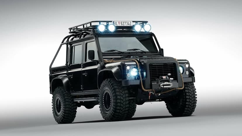 Black Land Rover Defender off-road truck with roof rack lights and thick tires on a white background.